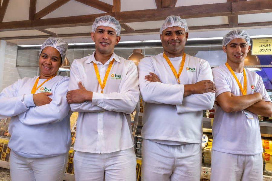Quatro funcionários de uniforme branco e touca, de braços cruzados, no OBA Hortifruti